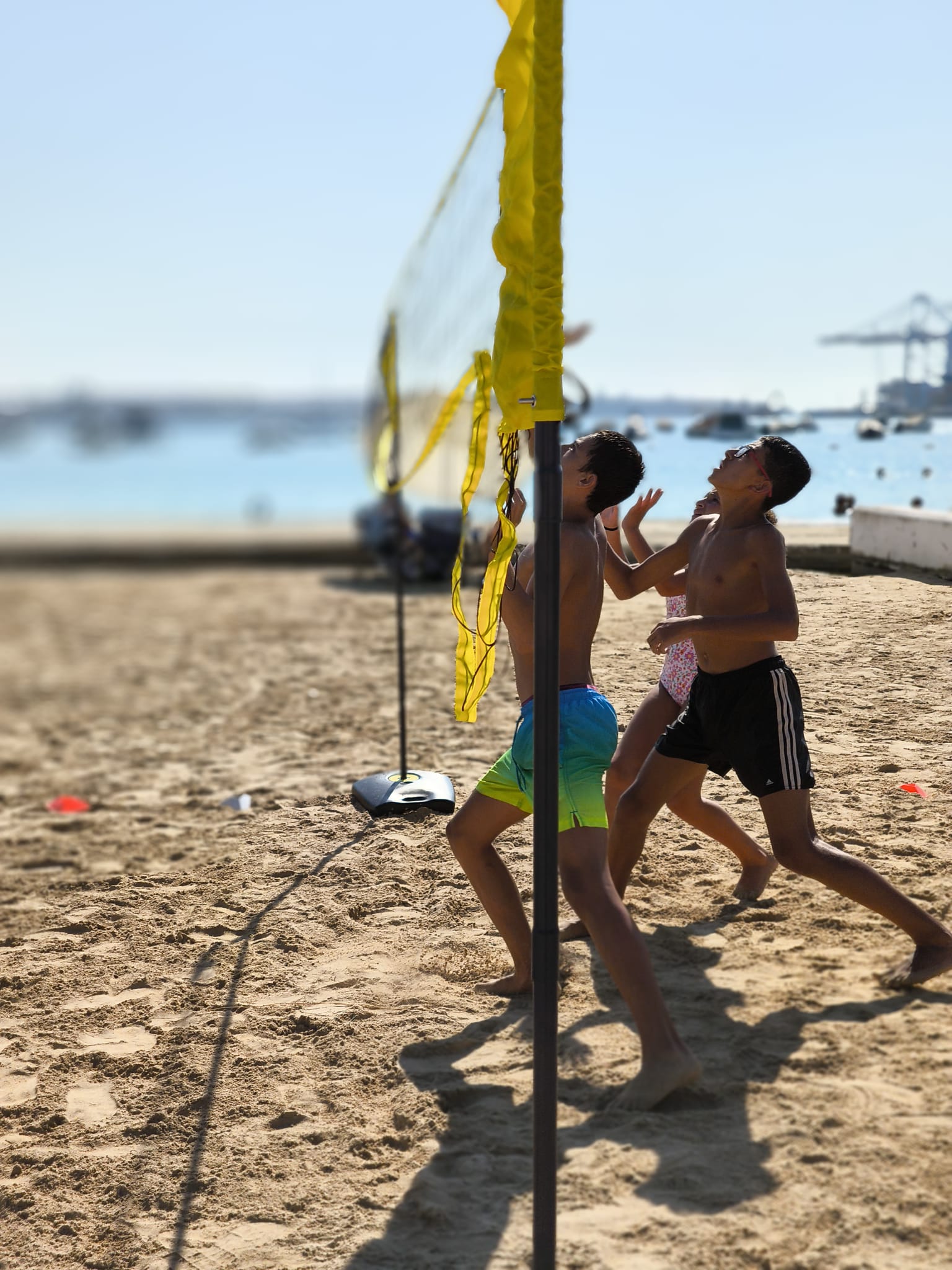 Players jumping and hitting a volleyball over the net on a sandy beach, with the ocean in the background
